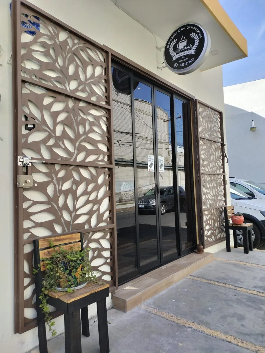 Fachada del local: puerta de cristal, celosía de hojas y letrero redondo negro
