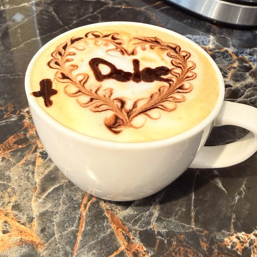 Capuchino con arte latte de chocolate: un corazón con la palabra Dulce y un signo de más